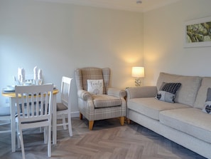 A living room with a sofa, a chair, a dining table with chairs, and a lamp.