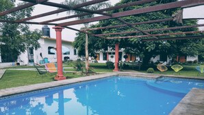 Une piscine surmontée d’une pergola, entourée d’une pelouse bien entretenue et d’un bâtiment à la façade blanche.