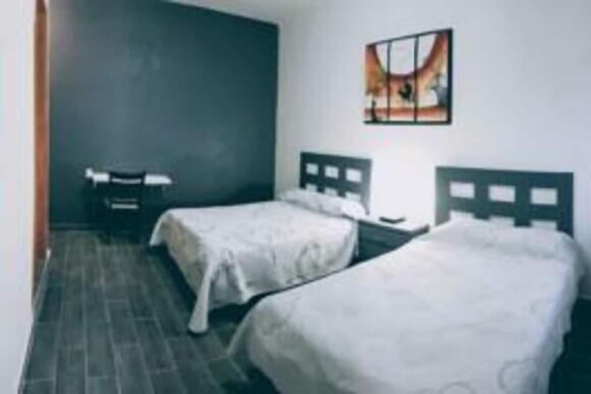 Una habitación con dos camas individuales, una mesita y una silla.