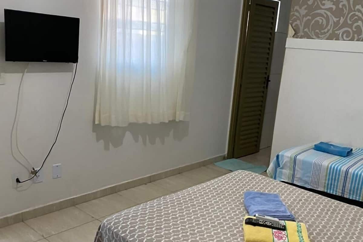 Ein Schlafzimmer mit einem Bett, einem an der Wand montierten Fernseher, einem Fenster mit Vorhängen und einer Klimaanlage.