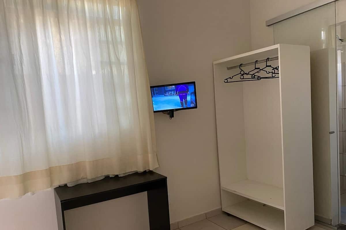 Ein Zimmer mit Fernseher auf einem Schrank, einer Bank, einem Kleiderschrank mit Kleiderstange und einer Tür.