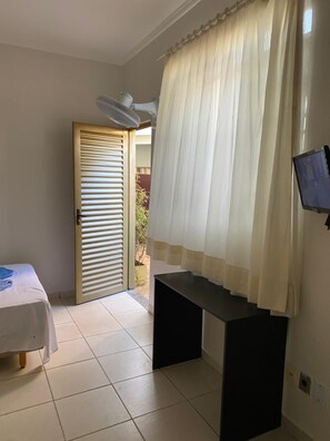 Une pièce comprenant un lit, un bureau, une télévision, un ventilateur de plafond et une porte donnant sur un espace extérieur.