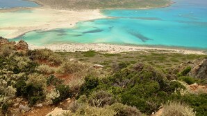 A coastal landscape with a sandy beach, clear turquoise waters, and a rocky hill in the background.