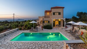 A two-story house with a swimming pool, outdoor seating, and a view of the sea.