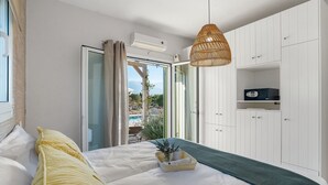 A bedroom with a bed, a wicker hanging light, a white wardrobe, and a view of a pool and mountains.