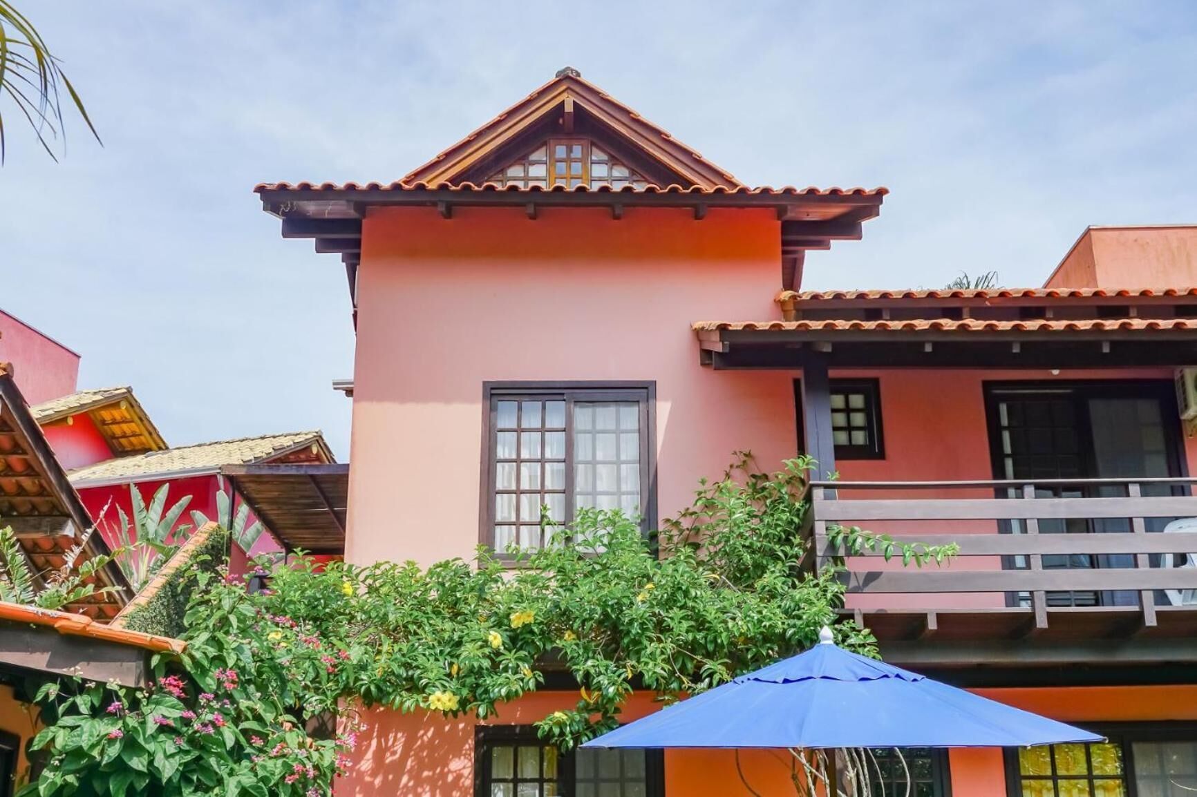 A pink building with a tiled roof, a window, and a balcony.