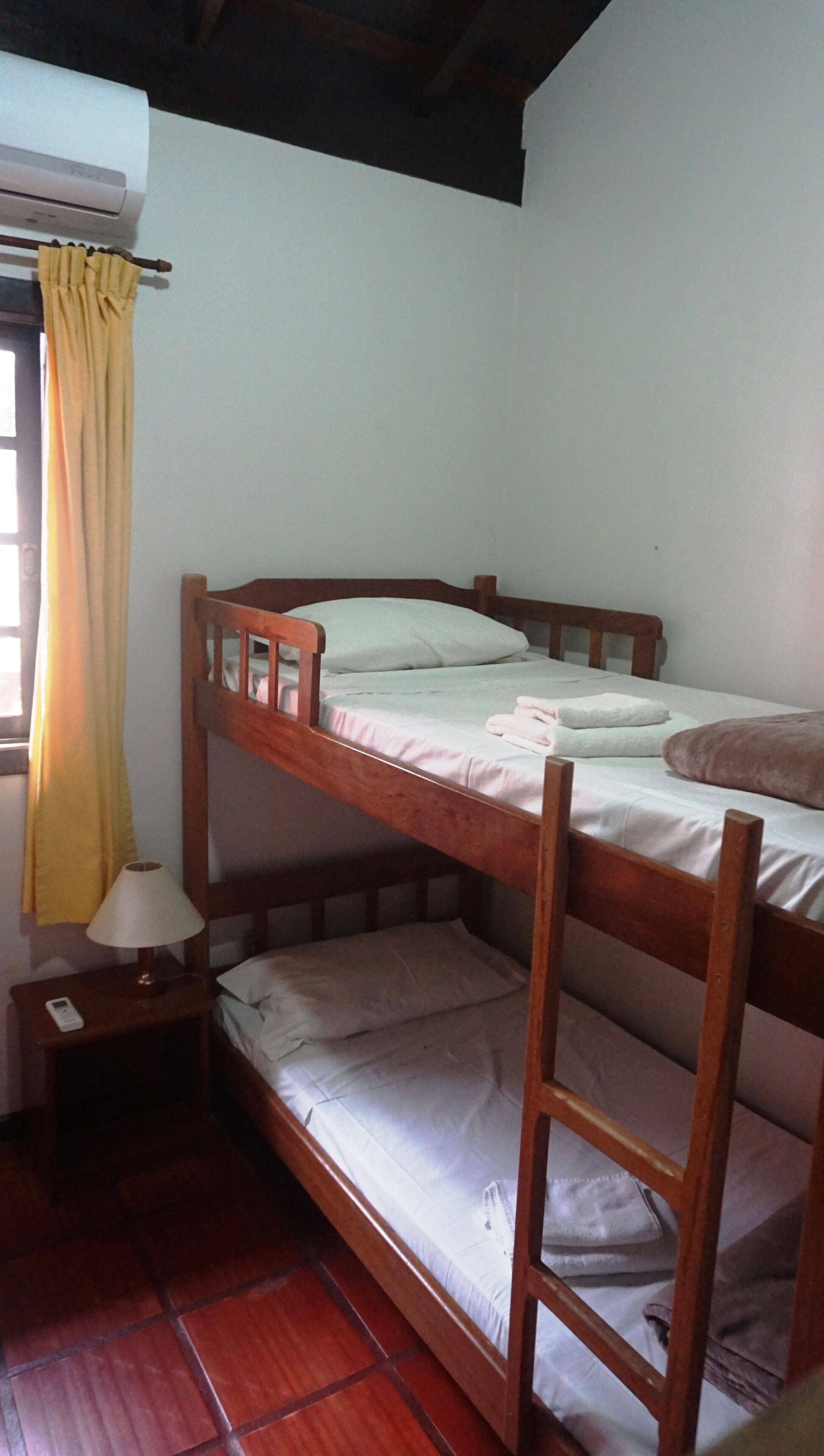 A bunk bed with a wooden frame, a bedside table with a lamp, and a window with curtains.
