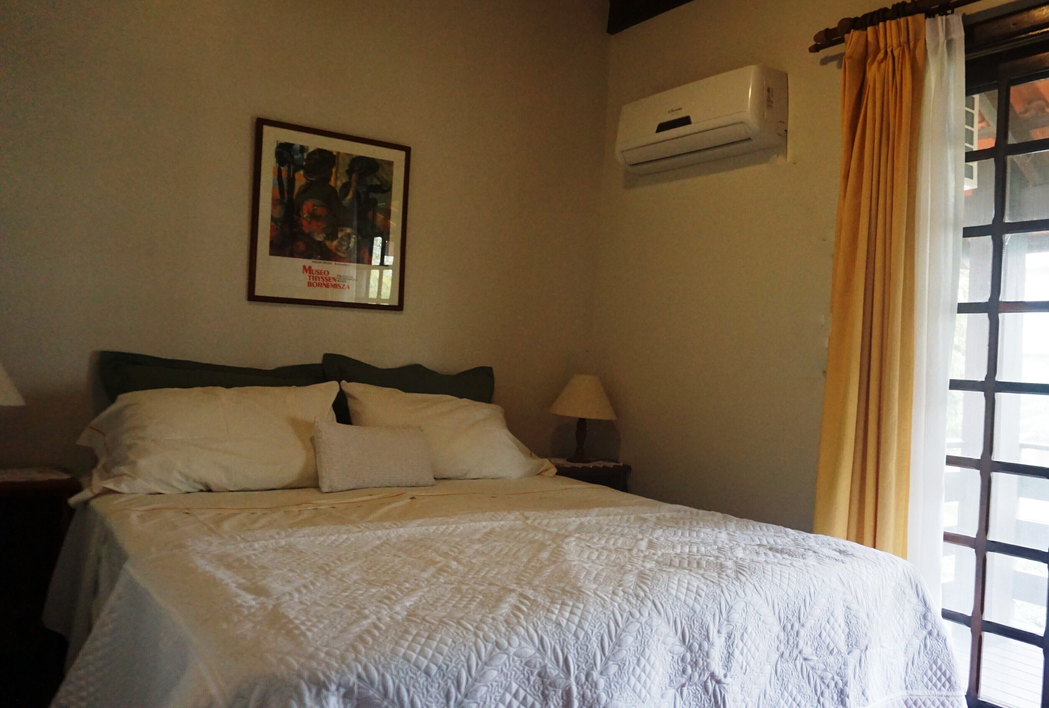 Ein Hotelzimmer mit einem Bett, einem Nachttisch, einer Lampe, einer Klimaanlage und einem Fenster mit Vorhängen.