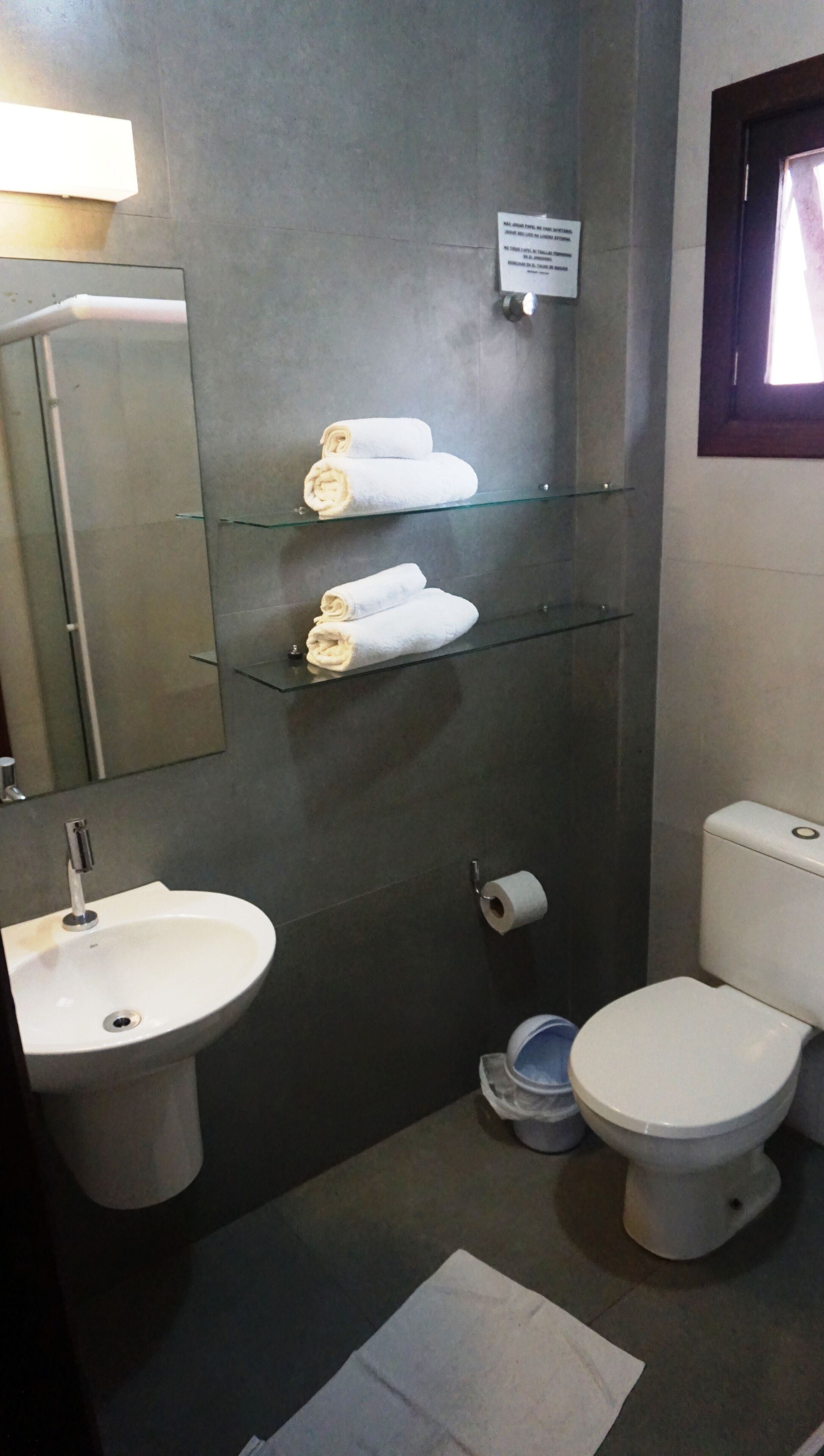 A bathroom with a sink, toilet, and two glass shelves holding rolled towels.