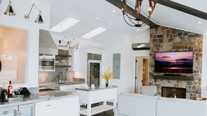 A modern kitchen with a stone fireplace, a flat-screen TV, and a cozy seating area. - Ocean View Penthouse (Carmel-by-the-Sea)