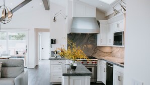 A modern kitchen with white cabinetry, a marble backsplash, and a central island. - Ocean View Penthouse (Carmel-by-the-Sea)
