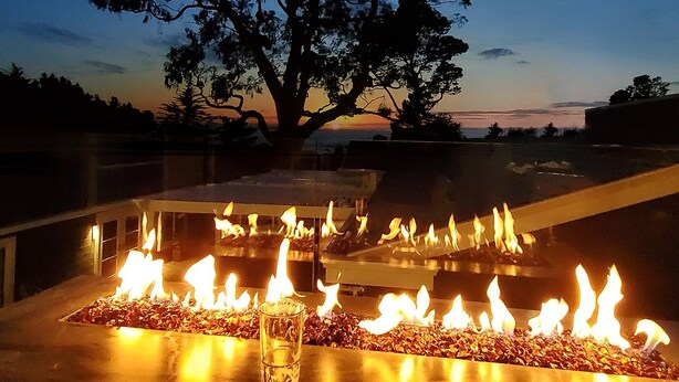 A fire feature with a glass enclosure and a tree in the background. - Ocean View Penthouse (Carmel-by-the-Sea)
