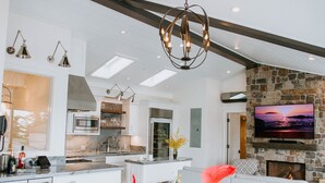 A modern kitchen with a stone fireplace, a flat-screen TV, and a dining area with a white sofa. - Ocean View Penthouse (Carmel-by-the-Sea)