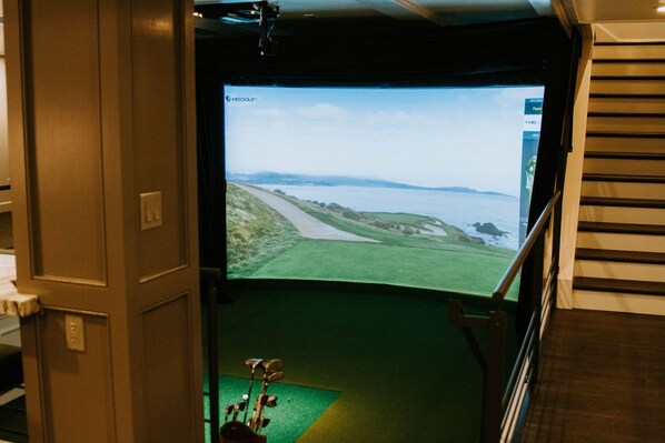 Una habitación con una pantalla grande que muestra un paisaje, un carrito de golf y una escalera.