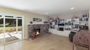 A spacious living room with a stone fireplace, a large bookshelf, and a sliding glass door leading to an outdoor patio.