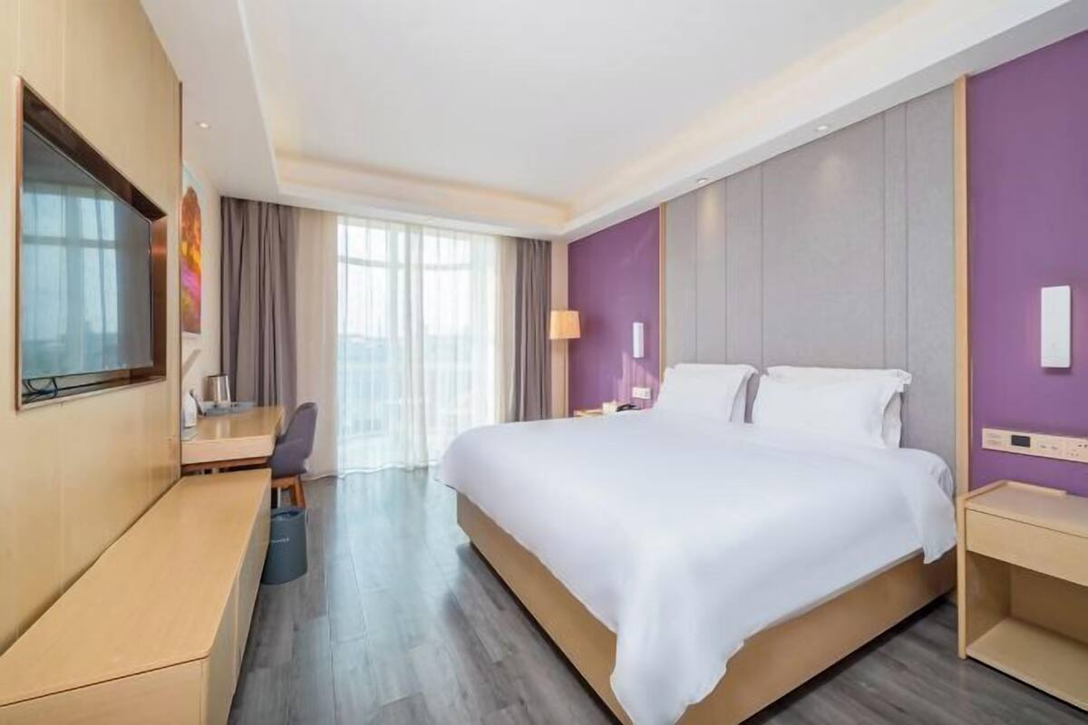 A modern hotel room with a large bed, a desk, a TV, and a view of the outdoors.