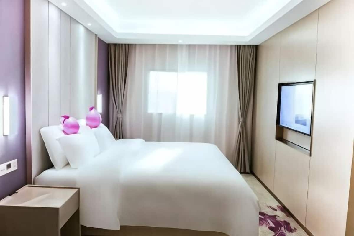 Ett hotellrum med en stor säng, en tv som är monterad på väggen och ett fönster med gardiner.