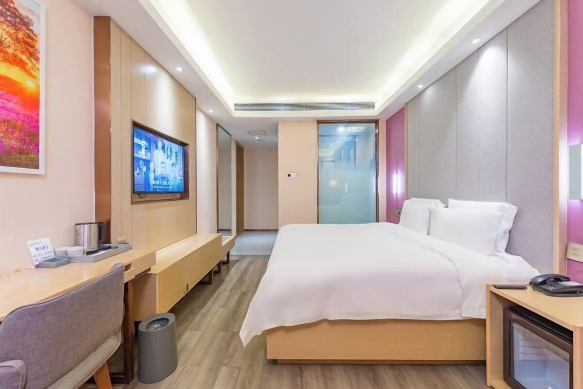 A hotel room with a bed, a desk with a chair, a TV, and a trash bin.