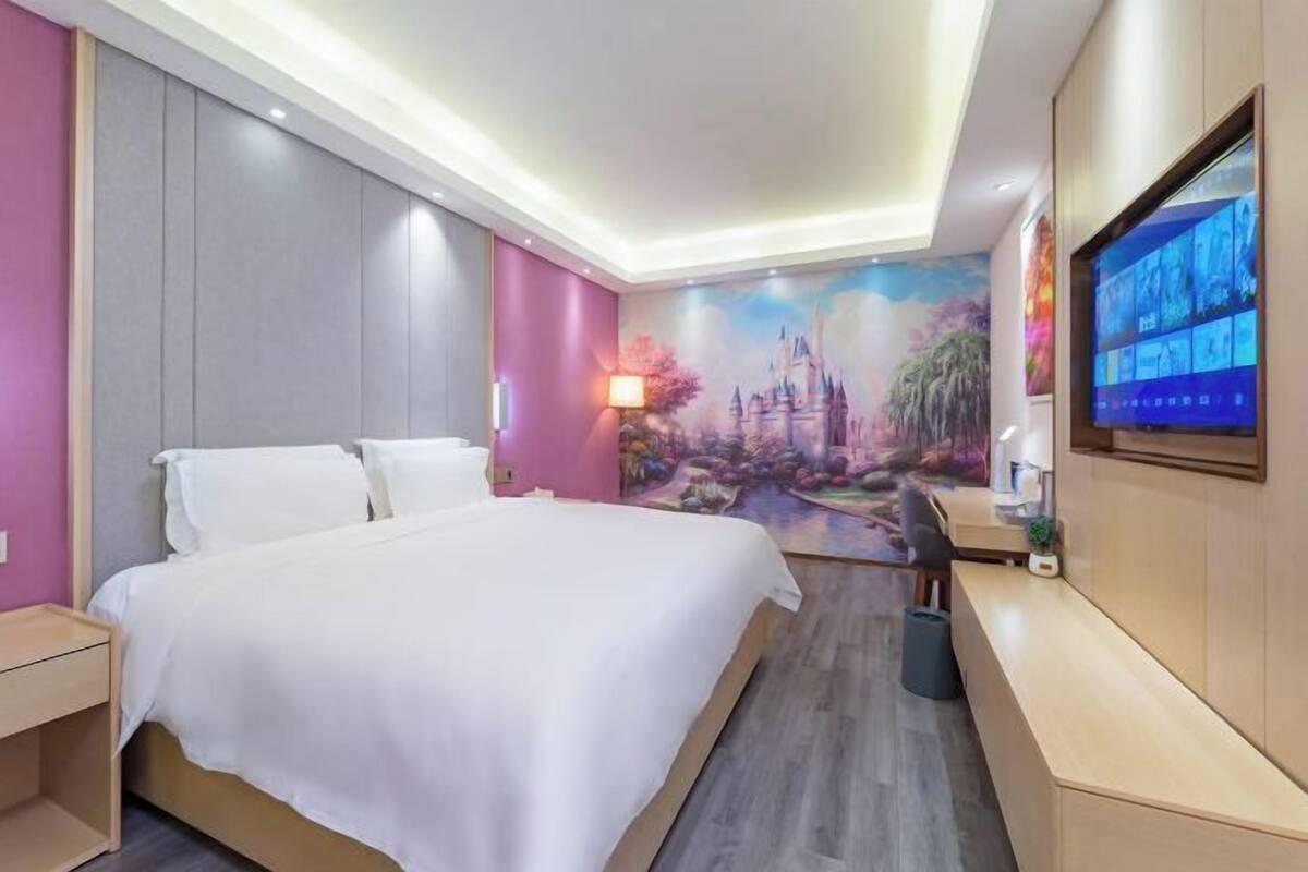 A hotel room with a bed, a desk, a TV, and a mural on the wall.