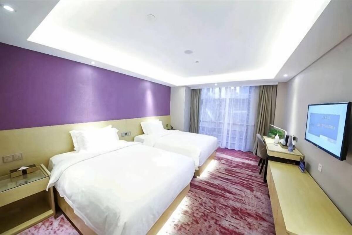 A hotel room with two beds, a desk, a TV, and a window with curtains.
