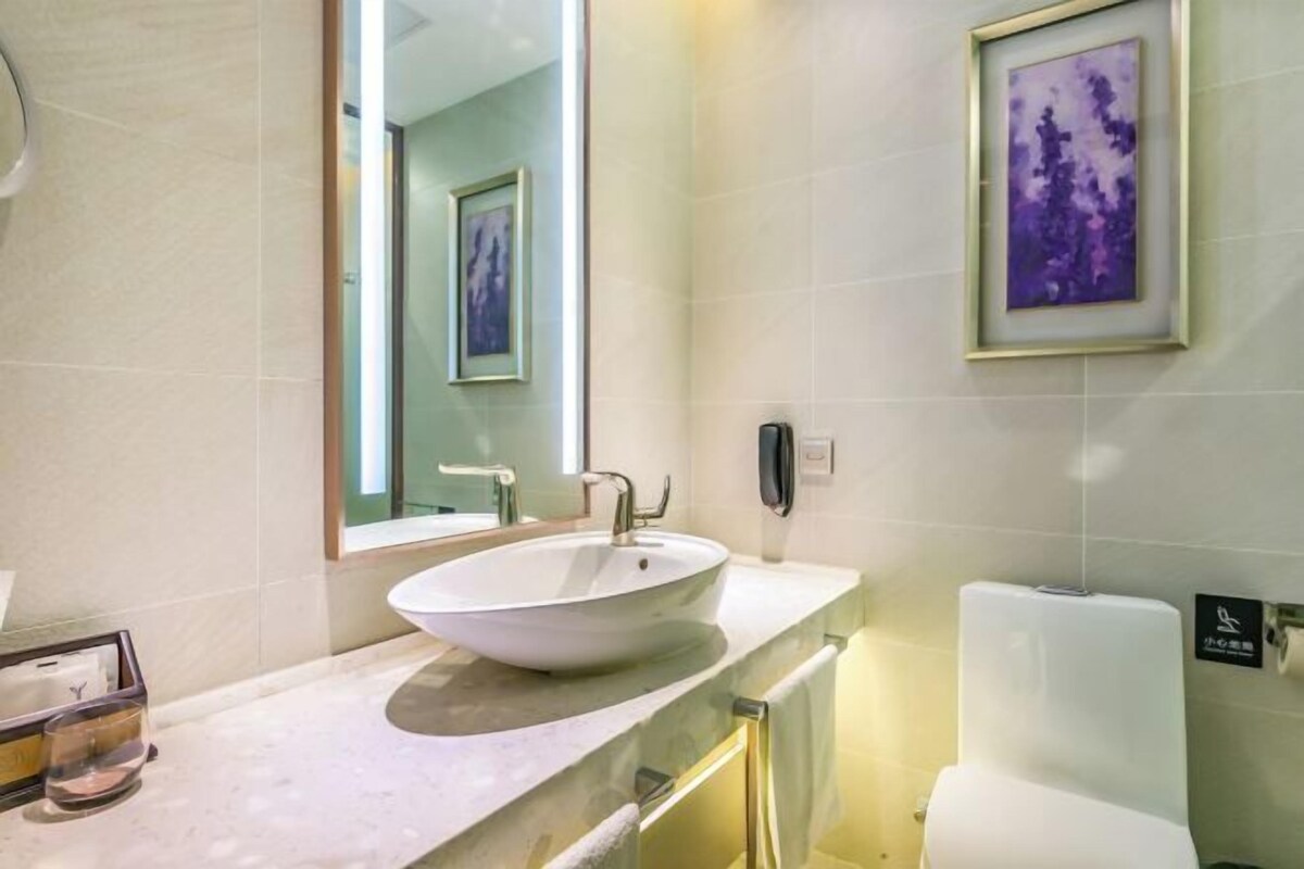 A modern bathroom with a large oval sink, a mirror, a framed artwork on the wall, and a toilet.