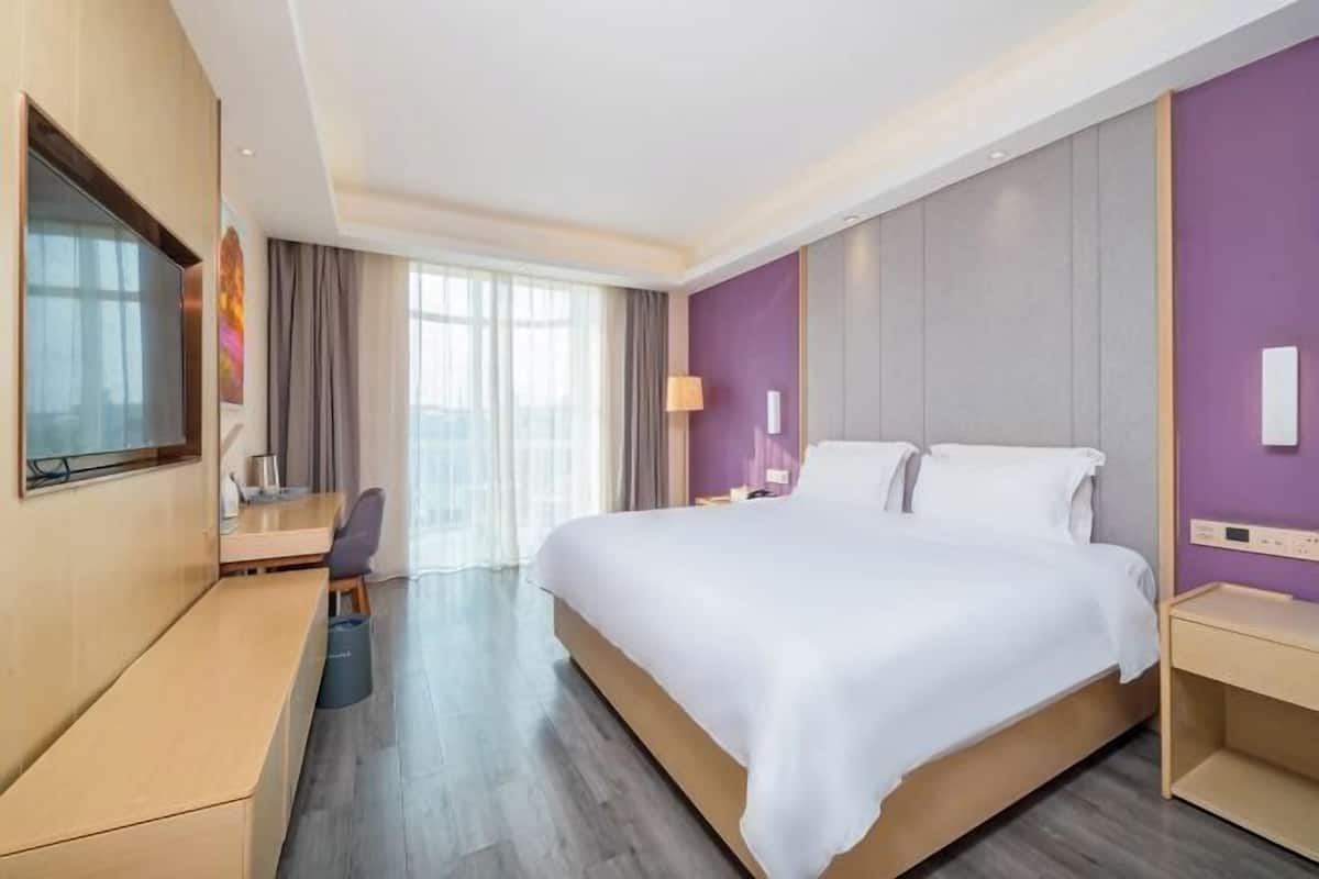 Ett modernt hotellrum med en stor säng, ett skrivbord, en TV och utsikt över omgivningarna.