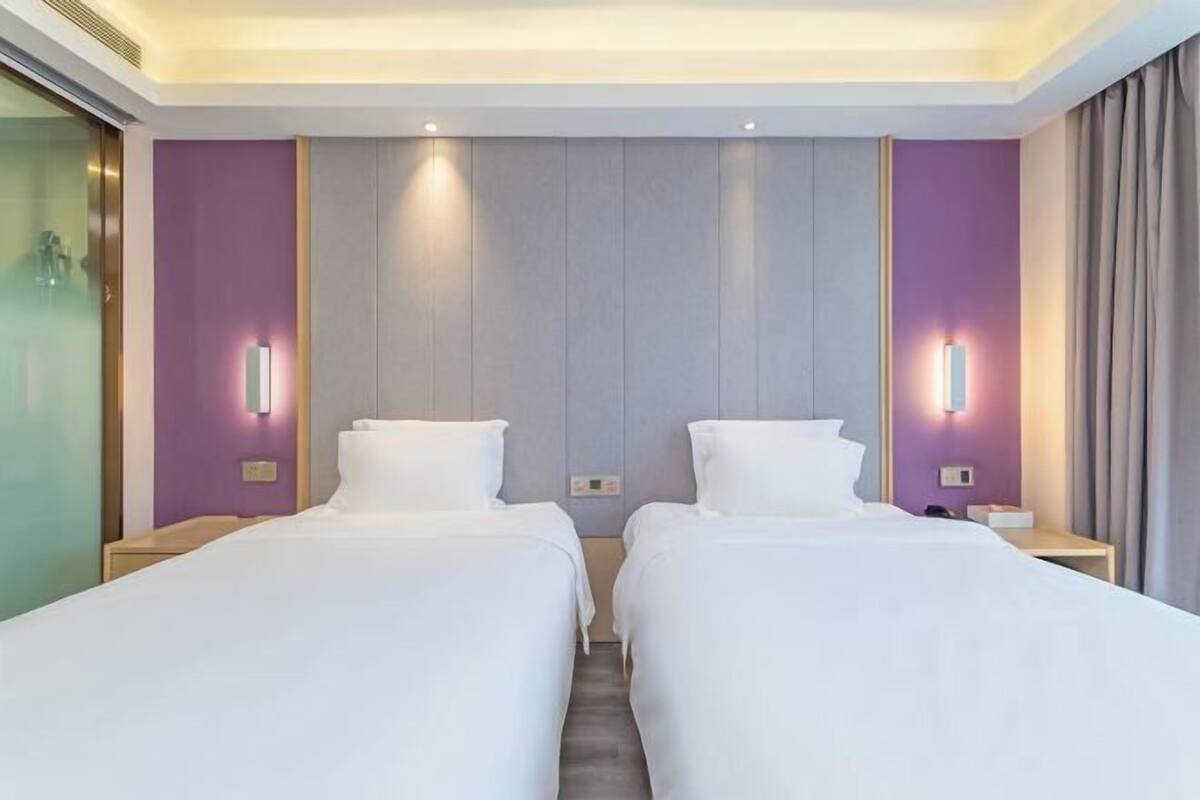 A hotel room with two beds, a large mirror, and wall-mounted lights.