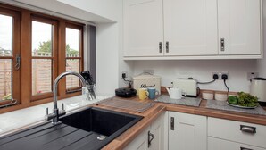 Uma cozinha moderna com pia preta, bancada de madeira, armários brancos e janela com vista para o exterior.