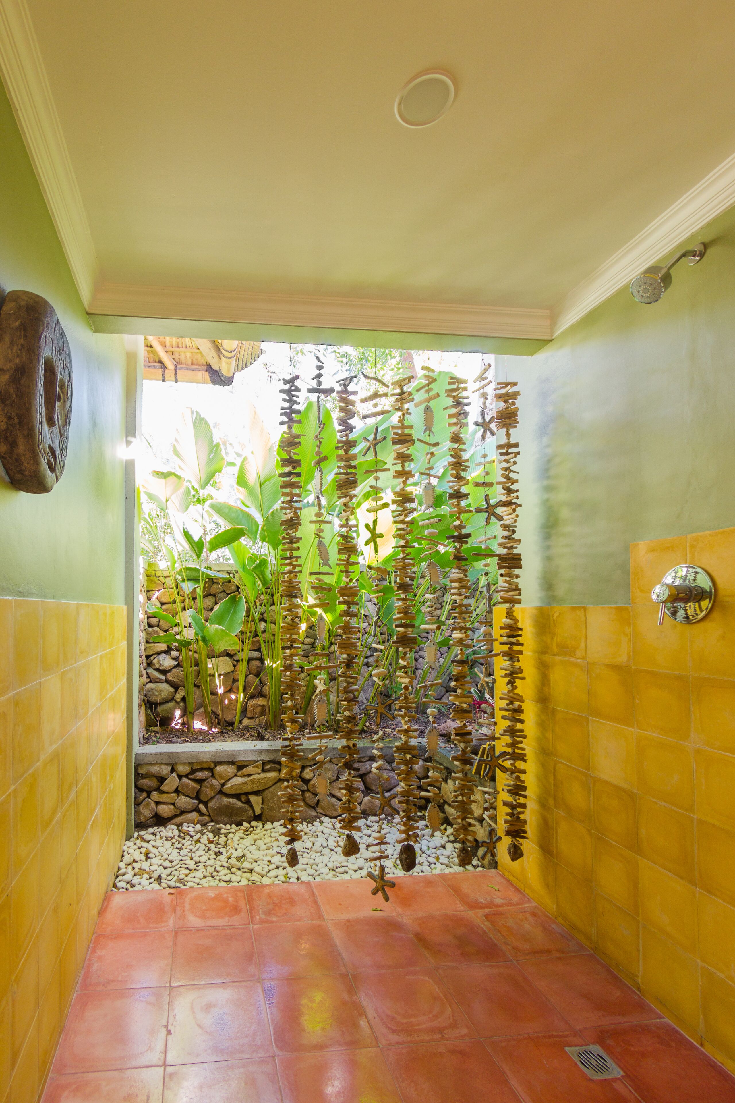 A shower area with a tiled floor, a stone wall, and a decorative plant arrangement.