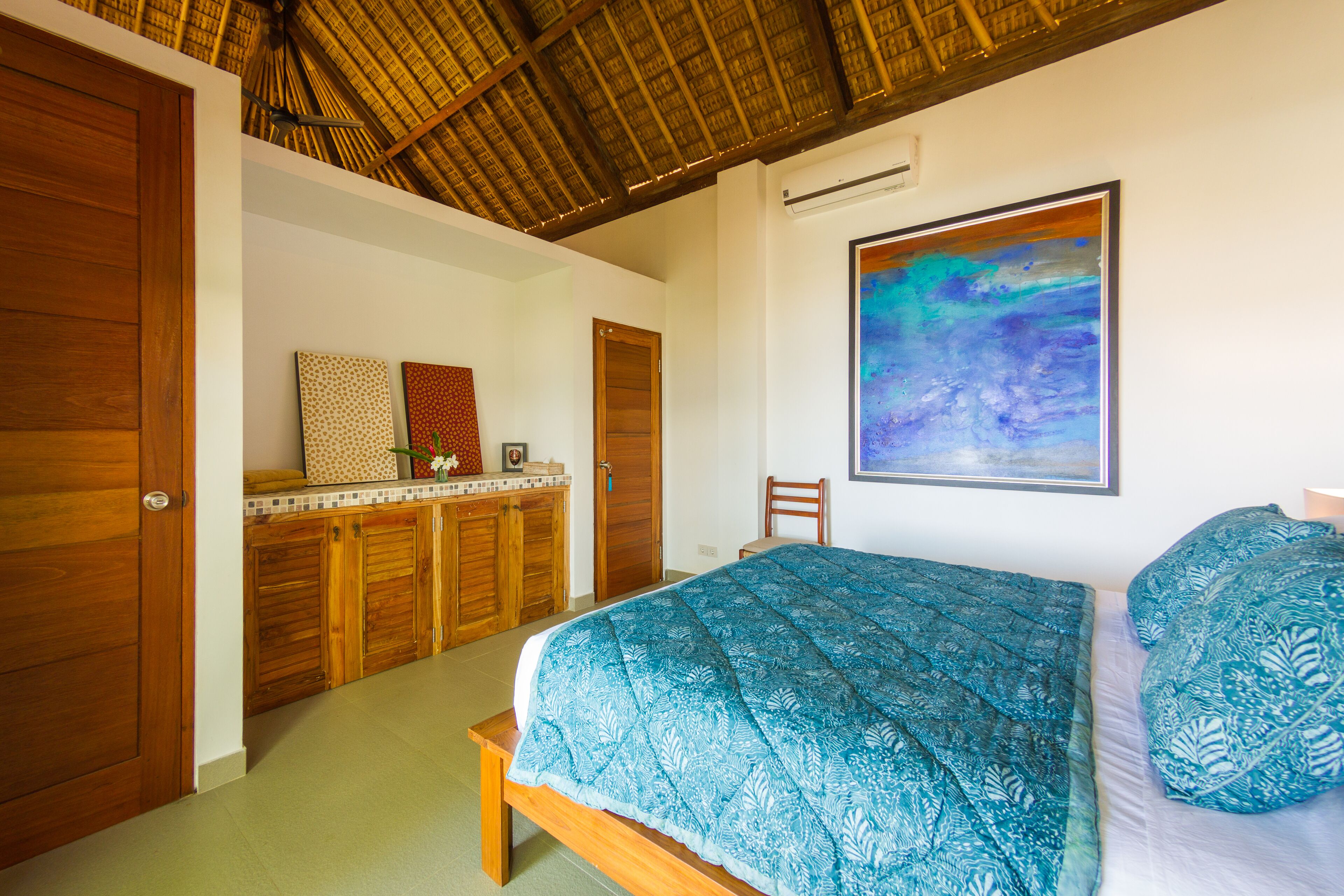 A bedroom with a bed, wooden wardrobe, and a painting on the wall.