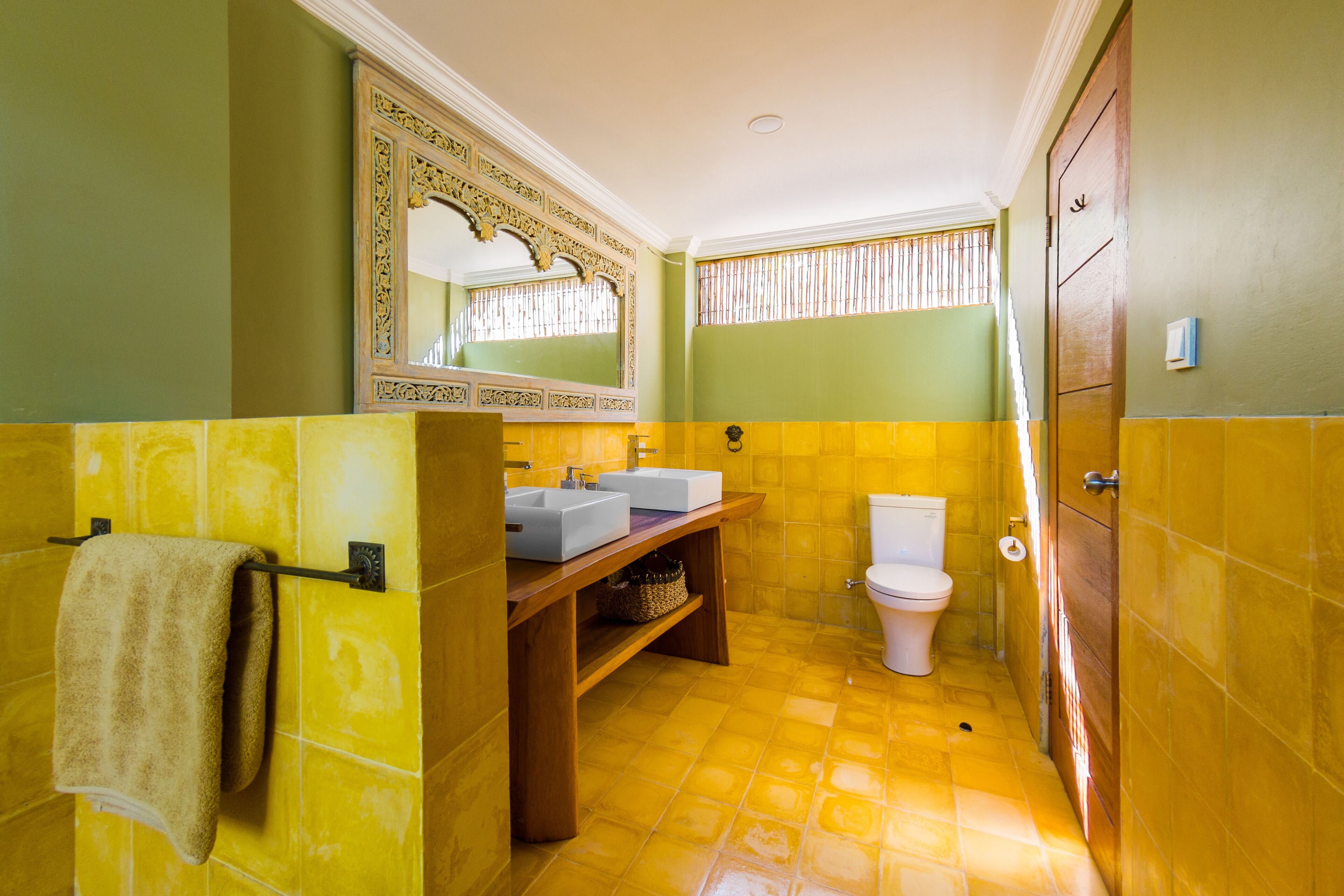 Un baño con azulejos amarillos, un mueble de tocador de madera, un espejo grande y un inodoro.