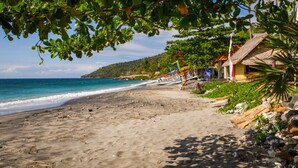 A beach with a thatched-roof building, a wooden walkway, and a view of the ocean. - Aquamarine Beach Villas (Karangasem)