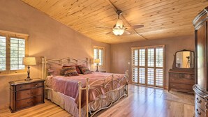 Quarto com teto de madeira, cama com estrutura de metal, mesa de cabeceira com gavetas, cômoda e espelho.
