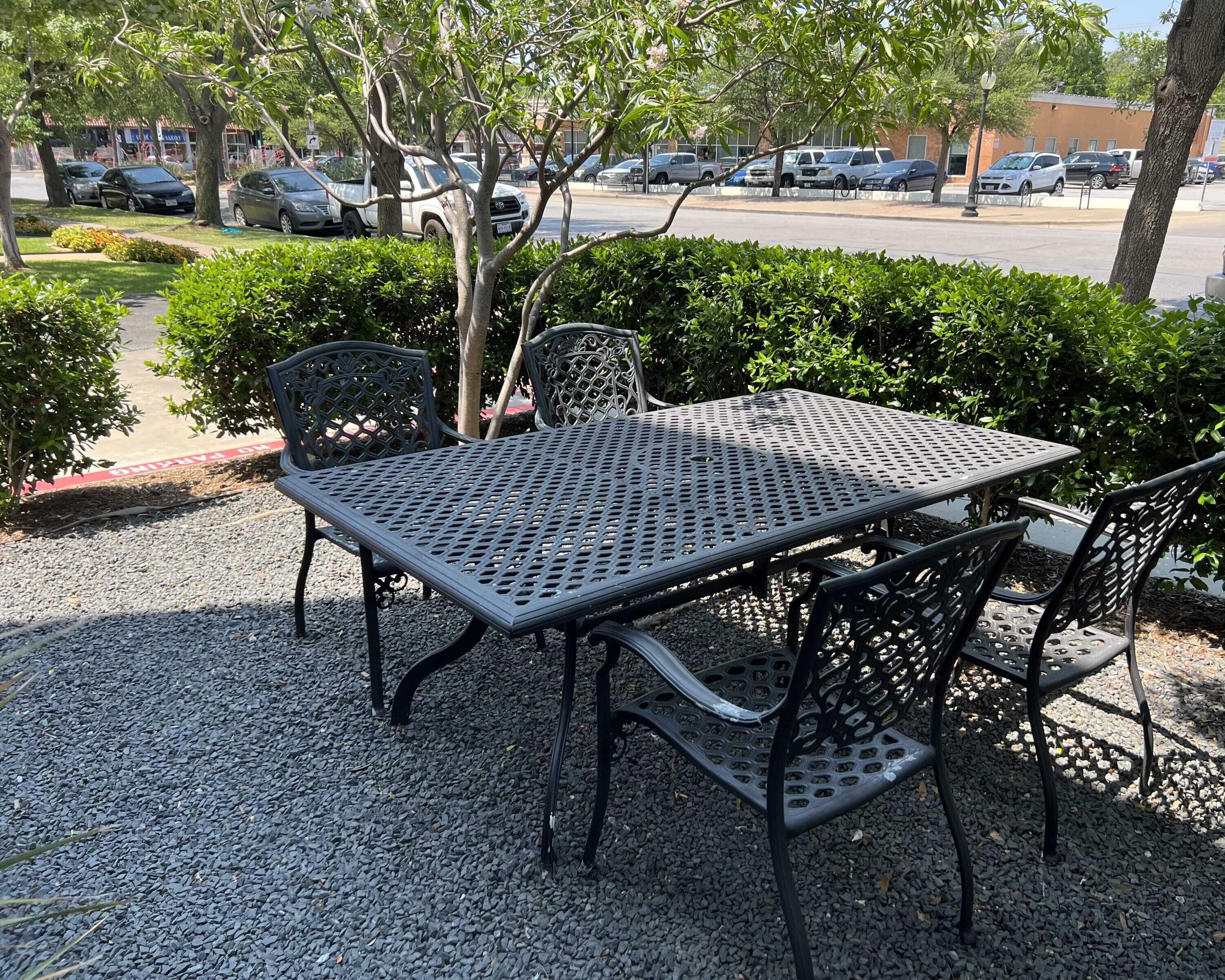 Un espace extérieur aménagé avec une table et des chaises en métal, entouré de gravier et de verdure.