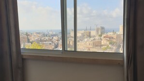 Ein Hotelzimmer mit Bett, einem Fenster mit Vorhängen und Blick auf eine Stadtlandschaft.