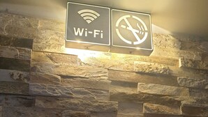 Eine Steinsäule mit zwei beleuchteten Schildern: eines für WLAN, das andere ein Rauchverbot.