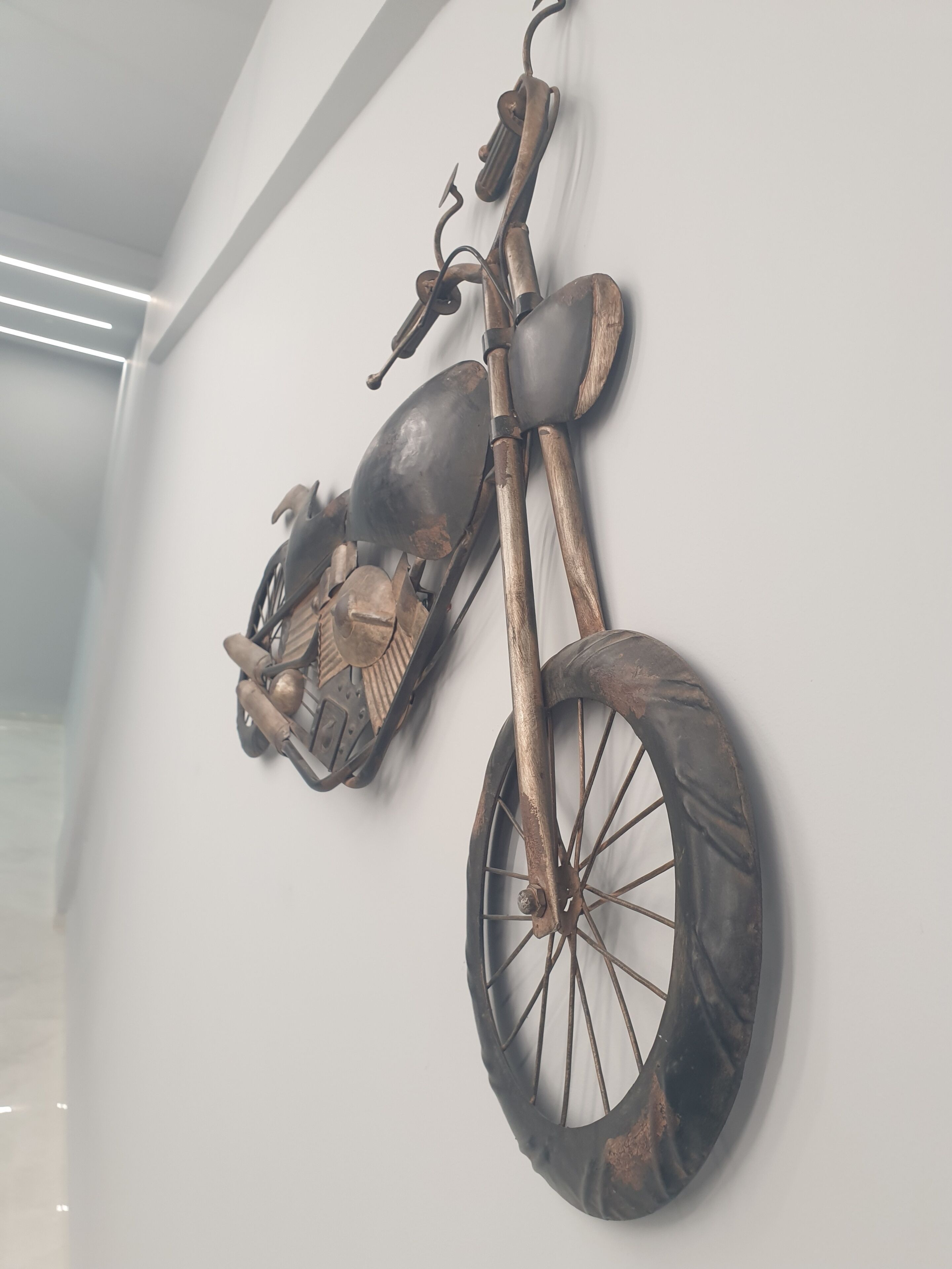 A wall-mounted motorcycle sculpture with a vintage design, including a headlight, handlebars, and a seat.