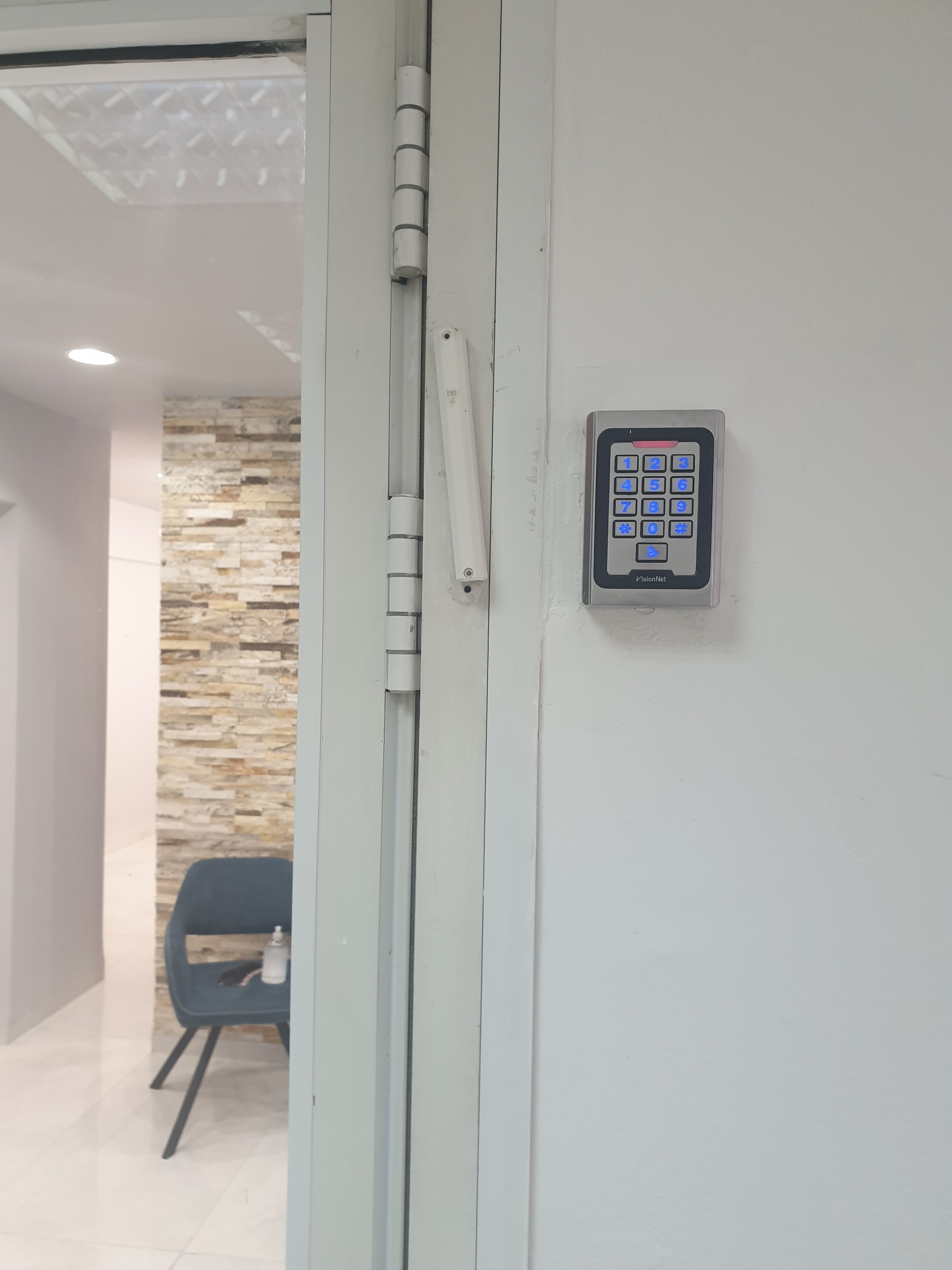 A door with a keypad lock, a stone wall, and a chair in a room.