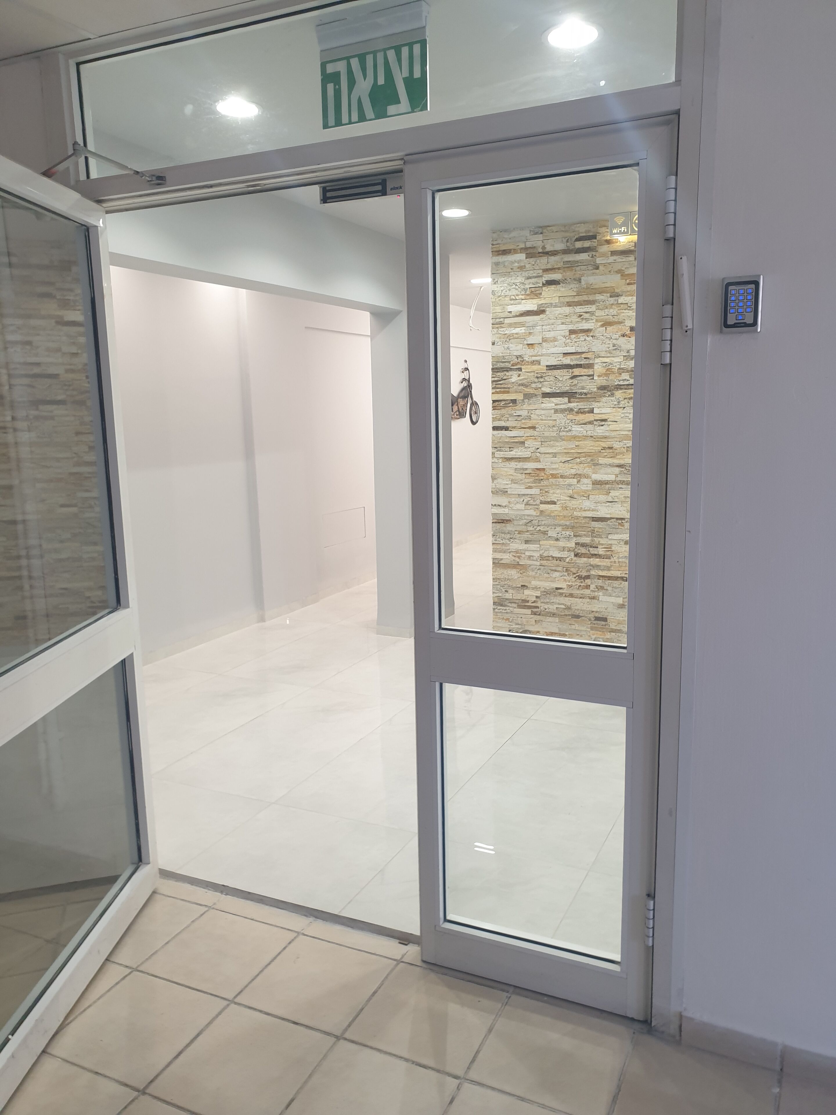 L’entrée d’un hôtel, avec une porte en verre, un système de verrouillage à clavier et un panneau indiquant la sortie.