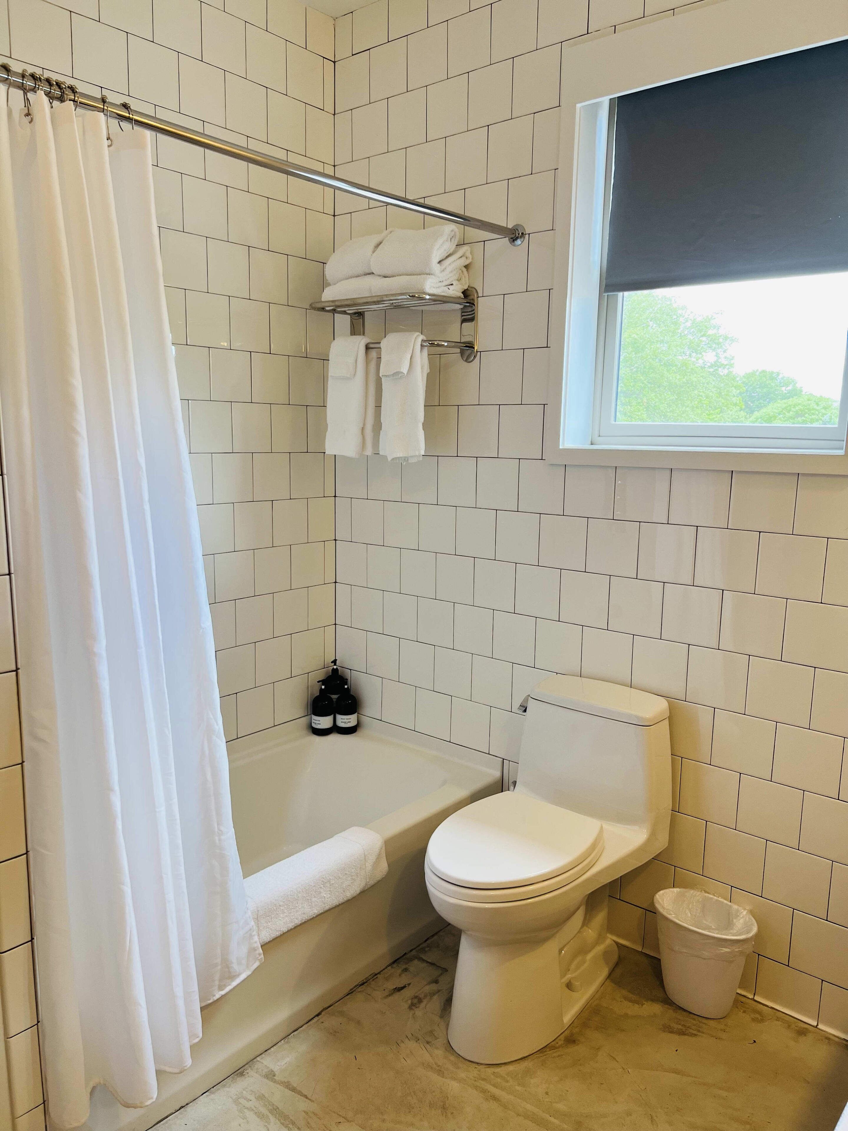 A bathroom with white tiles, a bathtub, a toilet, a window, and a shower curtain.