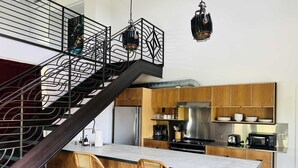 A modern kitchen with wooden cabinets, a stainless steel refrigerator, a built-in stove, and two wicker bar stools. - Bishop Arts Hotel Penthouse Suite 7 (Dallas)