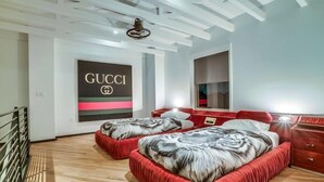 Een moderne slaapkamer met een houten vloer, een groot Gucci poster en een rode, gestoffeerde bed.