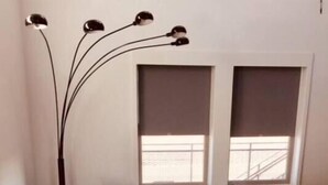 Een woonkamer met een visgraat parketvloer, een donkergroene bank met rode kussens, een ronde glazen salontafel en een vloerlamp met drie lampenkappen.