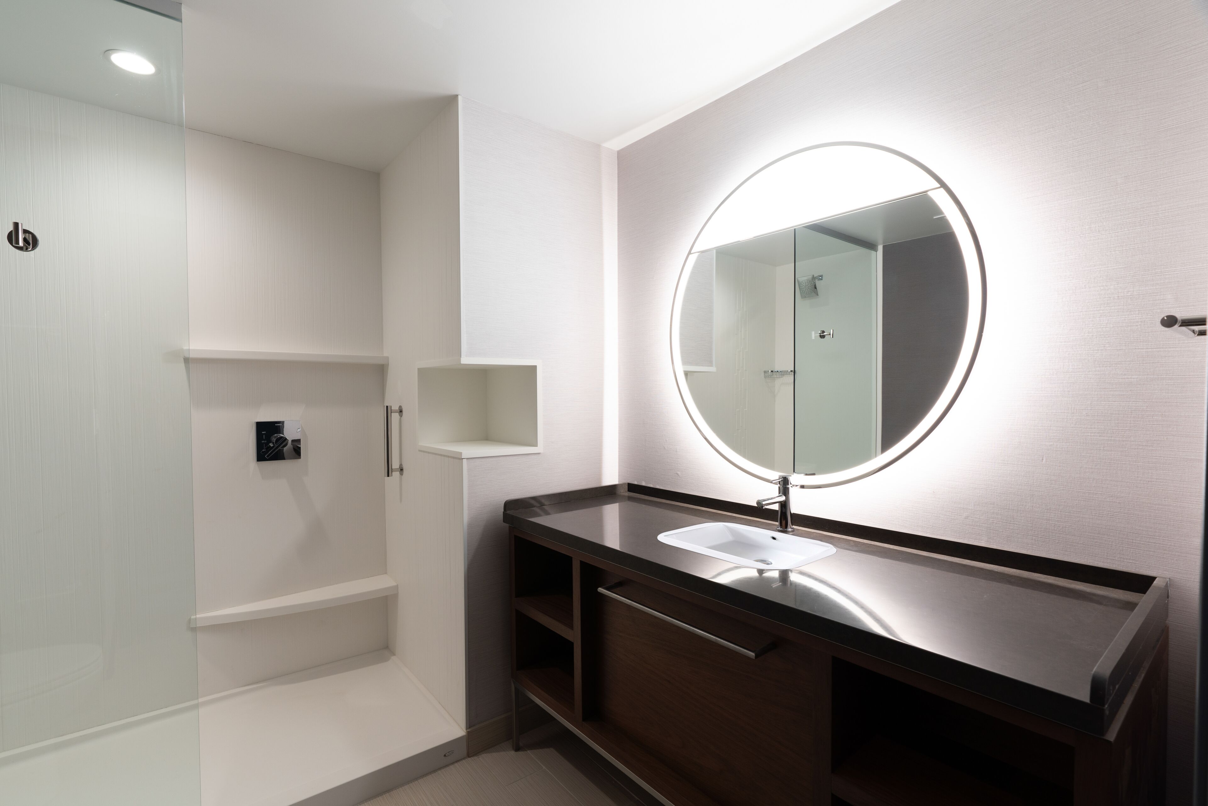 A modern bathroom with a round mirror, a sink, and a shower area.