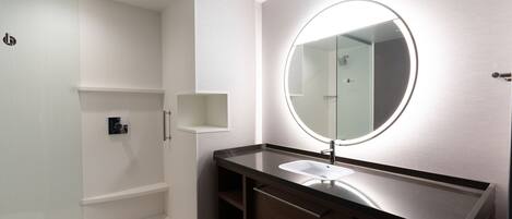 A modern bathroom with a round mirror, a sink, and a shower area.