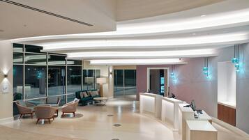 A modern lobby with a reception desk, seating area, and large windows.