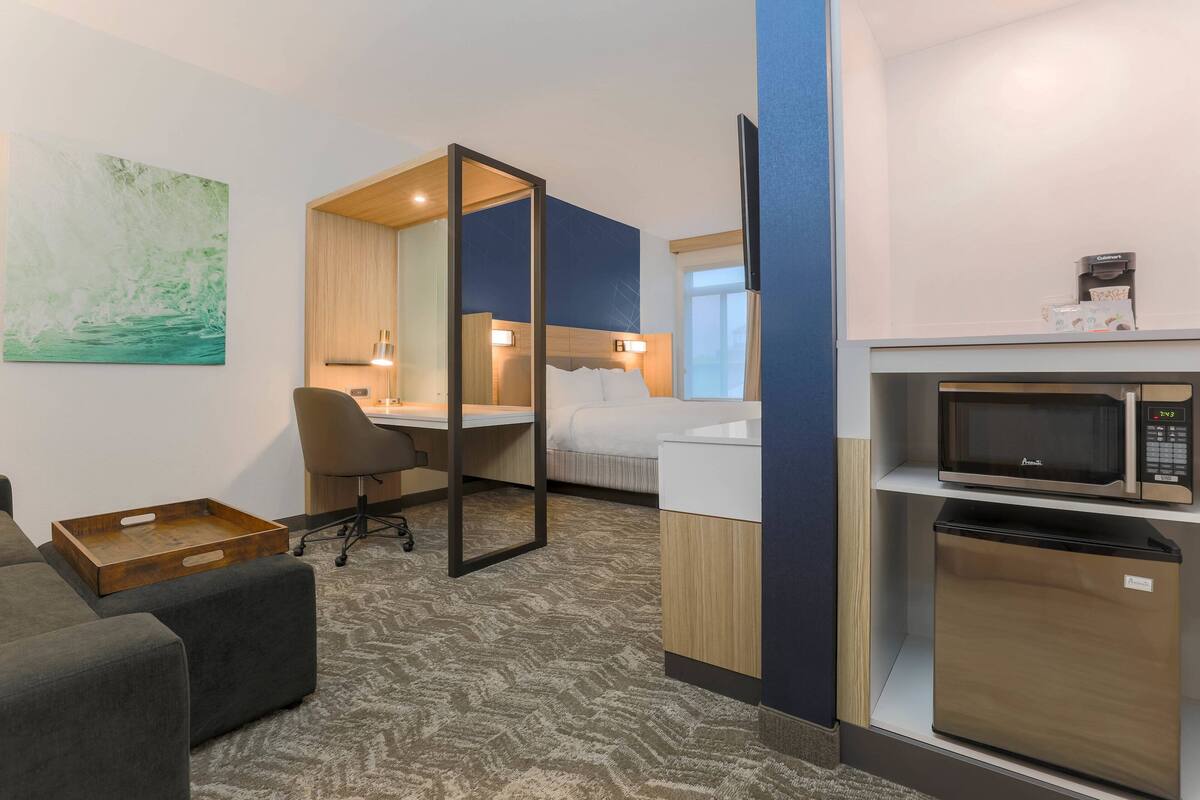 Ett hotellrum med en säng, ett skrivbord, en stol, en mikrovågsugn och ett litet kylskåp.