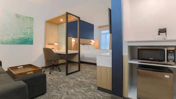 A hotel room with a bed, a desk, a chair, a microwave, and a mini-fridge.