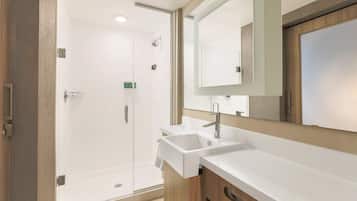 Un baño moderno con ducha de vidrio, lavabo blanco y un espejo grande.