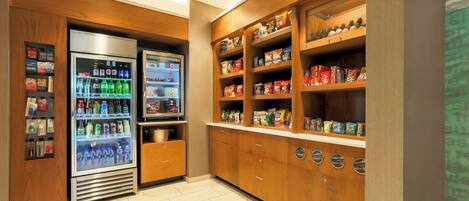 A kitchenette with a refrigerator stocked with beverages and snacks, wooden cabinets, and a microwave.